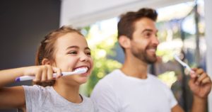 A father and daughter both brushing their teeth together